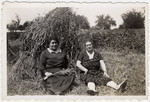 Two Alscatian Jewish women sit in a field next to a haystack.
