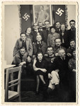 Group photograph posed in front of a portrait of Hitler and two swastikas.