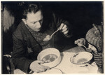 A father and son eat a bowl of soup in their kitchen in the Lodz ghetto.