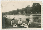 Three Jewish survivors relax by a river bed after the war.