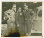 Three men pose beside an automobile in postwar Munich.