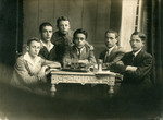 A photo of six young boys sitting and standing aroung a table.