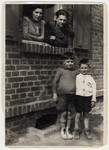Shanke and Shlamke Minuskin look out the window of their quarters in the Zeilsheim displaced persons' camp while their two boys, Henik and Kalman, stand below.