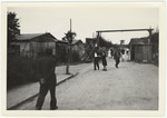 Displaced persons walk down the main street of their camp, probably a former concentration camp.