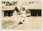 A female internee poses between two grass thatched huts in an interment camp for enemy aliens in Nyasaland.