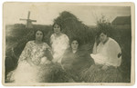 Four young Polish Jewish women sit amidst hay stacks.