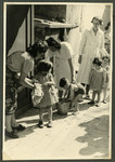 Staff of the Nos Petits kindergarten help young children wash their hands outdoors in a bucket.