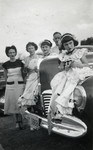 Postwar photo of Eva Meinberg dressed for Mardi Gras and sitting on an automobile.