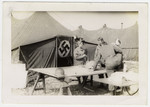 Group of American soldiers congregate in front of a tent displaying a Nazi flag as a door.