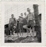 Four young Buchenwald survivors stand next to a barbed wire fence.