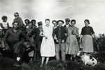 A group of thirteen people poses in front of a vineyard.