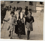An elderly Romani woman walks down a street accompanied by two girls.