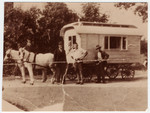 Three Romani men pose in front of a horse-drawn caravan.