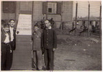 A group of survivors, including many children, stand in front of the barbed wire fence at the entrance to the Hanover-Ahlem concentration camp.
