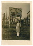 A young woman poses next to a sign for the Palestine Transit Camp.
