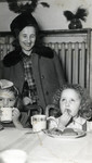 A woman stands next to two toddlers who are eating a meal in an unidentified children's home [perhaps Chez Nous].