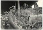 SS guard Schmiller walks past the barn of the Lipa farm labor camp where Jewish workers are pitching hay.