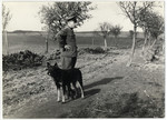 SS guard Schmiller stands on a dirt road in the Lipa farm labor camp with his dog.