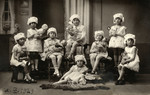 Studio portrait of kindergarten girls holding their dolls and wearing matching bonnets.