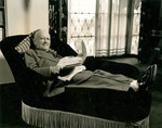 Hollywood producer Carl Laemmle rests on a couch reading a newspaper.