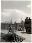 American GIs drive past and stand outside the wire fence surrounding the Ohrdruf concentration camp.