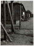 View taken from behind a barbed wire fence of female survivors sitting outside a barrack in the Ohrdruf concentration camp.