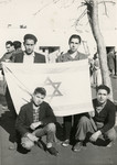Group portrait of youth in Mahane David, an immigration camp for North African Jews en route to Israel, holding an Israeli flag.