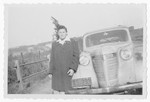 Bella Simon poses next to an automobile [possibly in postwar Romania.]
