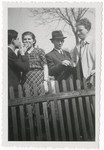 Four young people, two of them sharing a cigarette, stand behind a fence.