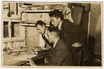 Three men gather around a desk in the statistical department of the Lodz ghetto.