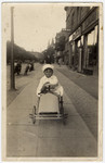 A young Jewish boy rides in a toy car on a sidewalk in Copenhagen.