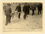 German civilians carry a corpse, using pieces of wood as a stretcher, from the Nordhausen concentration camp for burial.