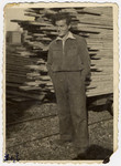 Close-up portrait of a young man standing in front of a stack of wooden boards.