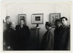 A group of men views an exhibition of paintings by artist Pinchas Szwarc (later Shaar).