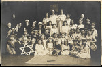 Jewish children dressed in costumes pose for a group portrait surrounded by large Stars of David.