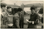 A Jewish policeman checks the documents of several men at the entrance of the central prison of the Lodz ghetto [probably prior to their deportation].