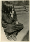 A destitute girl sits on the curb of a street of the Lodz ghetto.