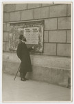 A religious Jew studies a Polish bulletin about a school pasted on the wall of a building.