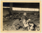 A survivor sits on a stool inside a barrack in Nordhausen, surrounded by corpses.