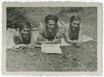 Three Polish Jewish young adults sunbathe on a lawn.