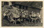 Dutch Jewish children gather around two picnic tables in a summer school camp in The Netherlands.