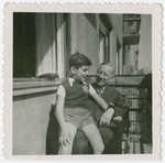Otto Veidlinger, sits on the lap of his father, on the balcony of their apartment; in Budapest; both are wearing Jewish stars.