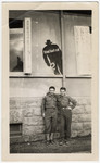 Two American soldiers pose underneath a poster that shows a lurking silhouette and a German caption that reads "The enemy is listening."