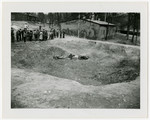 Corpses lie in a sunken mass grave outside a barrack of the Langenstein-Zwieberge concentration camp while survivors gather nearby.