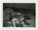 A survivor lies on the ground of a barrack of the Langenstein-Zweiberge concentration camp among rags, uniforms, and other items.