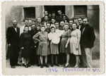 A large group of men and women, including several pregnant women and one holding an infant, pose outside 10 Tennesse Street in the Foehrenwald displaced person's camp.