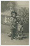 Studio portrait of Mietek Juress as a young boy posing with a hobby horse.