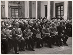 Adolf Hitler and other Nazi officials gather in a large room lto listen to a speaker.