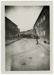 Survivors walk down a road of [what is probably the Buchenwald concentration camp] with barracks on either side.