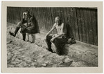 Two survivors rest against the side of a barrack following liberation.